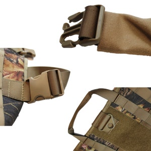 May include: A camouflage dog harness with adjustable straps and a buckle closure. The harness has a brown padded chest piece and a handle on the top.