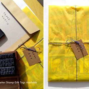 May include: A yellow gift wrap with a blue ribbon and a brown gift tag that says "Love Zac". The gift wrap is on a white surface. The gift tag is tied to the ribbon with a blue string. The gift wrap is made of tissue paper. The gift tag is made of brown paper. The gift tag is tied to the ribbon with a blue string. The gift wrap is on a white surface.