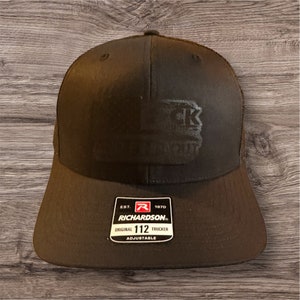 May include: Black trucker hat with a black embroidered logo that says "Blackout" on the front. The hat is adjustable and has a Richardson label on the back.