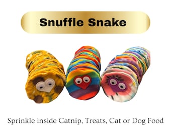 May include: Three colorful Snuffle Snakes for pets. Each snake is made of soft fabric and features a whimsical face with googly eyes. The text "Snuffle Snake" is above the snakes, and the text "Sprinkle inside Catnip, Treats, Cat or Dog Food" is below.