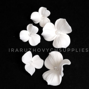 May include: White ceramic flower embellishments scattered on a black background. The flowers have multiple petals and a small, central detail. The image includes the text "IRARUZHOVYCHSUPPLIES".