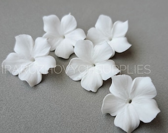 May include: Five white paper flowers with five petals each. The flowers are arranged in a semi-circle on a gray surface.