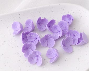 May include: A collection of 15 light purple flower petals made of polymer clay. The petals are scattered on a white surface.