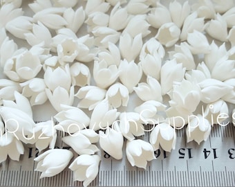 May include: A pile of white, paper flower buds, approximately 1/2 inch in size, scattered on a white surface with a ruler in the foreground. The ruler is marked in inches.