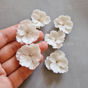 Puede incluir: Seis flores de papel blancas con una superficie ligeramente texturizada. Las flores están dispuestas en una mano.