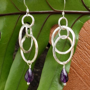 May include: Silver dangle earrings with multiple interlocking circles and a teardrop-shaped amethyst gemstone pendant.