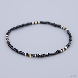 Könnte beinhalten: Ein schwarzes Armband mit goldenen und silbernen Akzenten.
