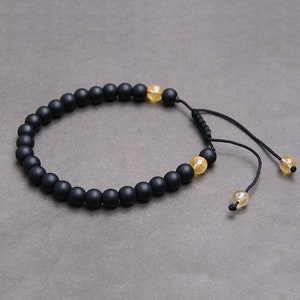 May include: A black beaded bracelet with a sliding knot closure. The bracelet features small, round, black beads and two larger, round, yellow beads.