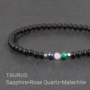 Puede incluir: Un brazalete de cuentas negras con un dije de piedras preciosas de zafiro, cuarzo rosa y malaquita. El brazalete está etiquetado como "TAURUS Sapphire.Rose Quartz.Malachite".