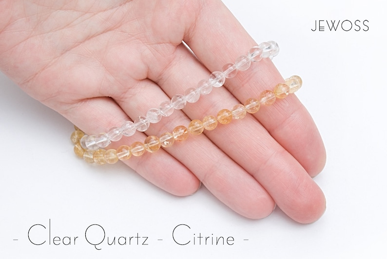 May include: Two beaded bracelets, one clear quartz and one citrine, rest on a hand. The clear quartz bracelet is transparent, while the citrine bracelet has a warm, golden-yellow hue. The image includes the text "- Clear Quartz - Citrine -" in a handwritten font.
