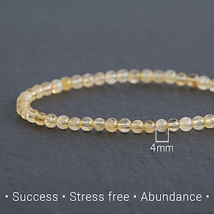 May include: A delicate bracelet made of small, round, yellow-orange beads. The beads are approximately 0.16 inches in diameter. The image includes the text "Success • Stress free • Abundance."