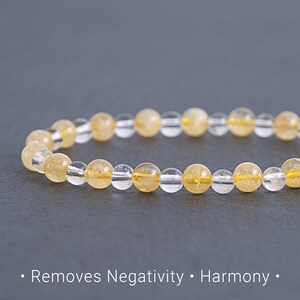May include: A beaded bracelet featuring alternating clear and yellow-toned gemstones. The yellow stones are evenly spaced among the clear beads. The text at the bottom of the image reads: Removes Negativity • Harmony.