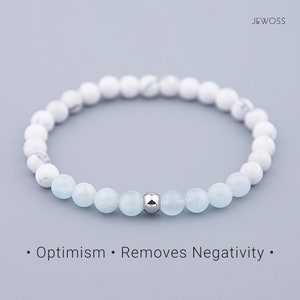 May include: A beaded bracelet featuring white and light blue gemstones, with a silver accent bead. The bracelet is strung on an elastic band. Text on the image reads: "Optimism • Removes Negativity."