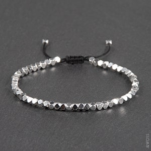 May include: A silver beaded bracelet with a black adjustable cord. The beads are hexagonal in shape and have a metallic finish.