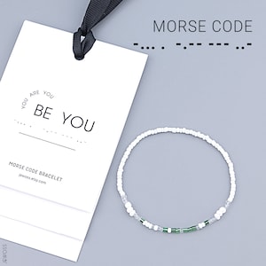Puede incluir: Pulsera de cuentas blancas con cuentas verdes, una tarjeta con el texto "You are You Be You" y las palabras "Morse Code Bracelet" y el sitio web "jewoss.etsy.com".