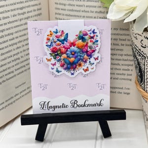 May include: A pink and white magnetic bookmark with a heart-shaped design featuring a colorful butterfly and flower arrangement. The bookmark has the text "T2T" printed on it and the words "Magnetic Bookmark" at the bottom.