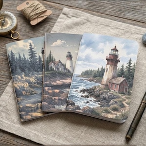 May include: Three notebooks with lighthouse illustrations, featuring a red and white lighthouse, are displayed on a wooden surface. The notebooks are accompanied by a pen, ink bottle, compass, and twine.