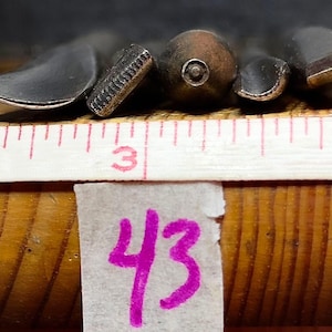 May include: A set of five metal carving tools with various tip shapes, including gouges and chisels, positioned behind a white measuring tape showing a scale in centimetres. A small white paper tag with the handwritten number 43 is attached below.