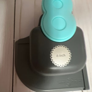 Könnte beinhalten: Ein grauer und hellblauer Papierstanzer mit einem 6 Zoll Etikett. Der Stanzer ist in Form der Zahl Acht.