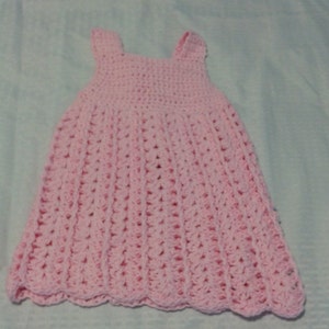 May include: A pink crocheted baby dress with a scalloped hem.