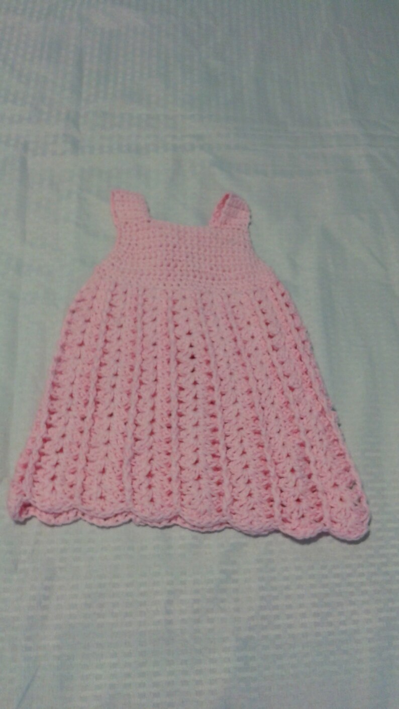 May include: A pink crocheted baby dress with a scalloped hem.