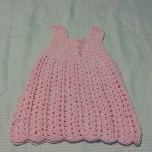 May include: A pink crocheted baby dress with a scalloped hem.
