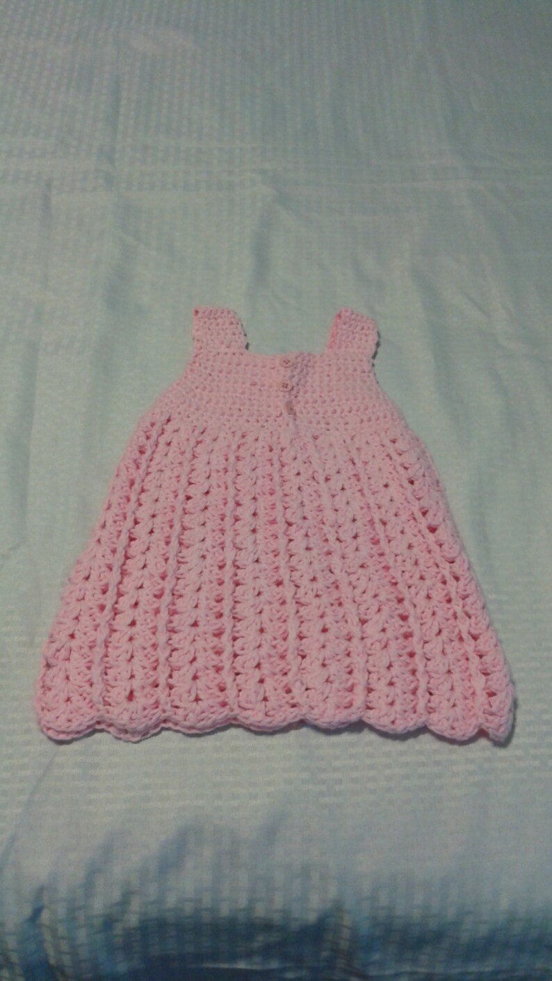 May include: A pink crocheted baby dress with a scalloped hem.