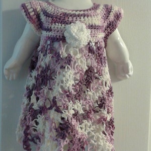 May include: A purple and white crocheted dress with a flower detail, displayed on a white doll form.