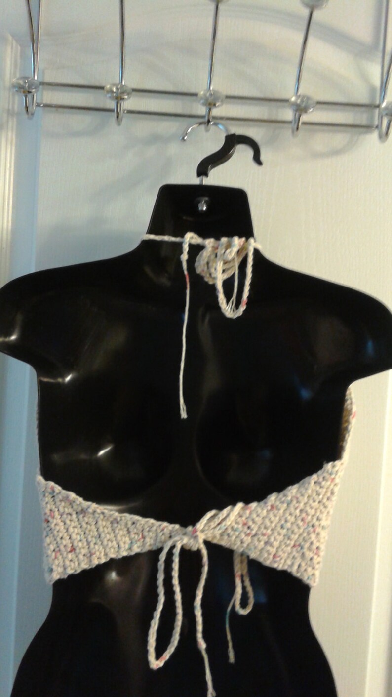 Puede incluir: Un top halter blanco de ganchillo con un patr&oacute;n moteado multicolor. El top tiene tirantes ajustables que se atan en la parte posterior del cuello y en la parte delantera de la cintura.