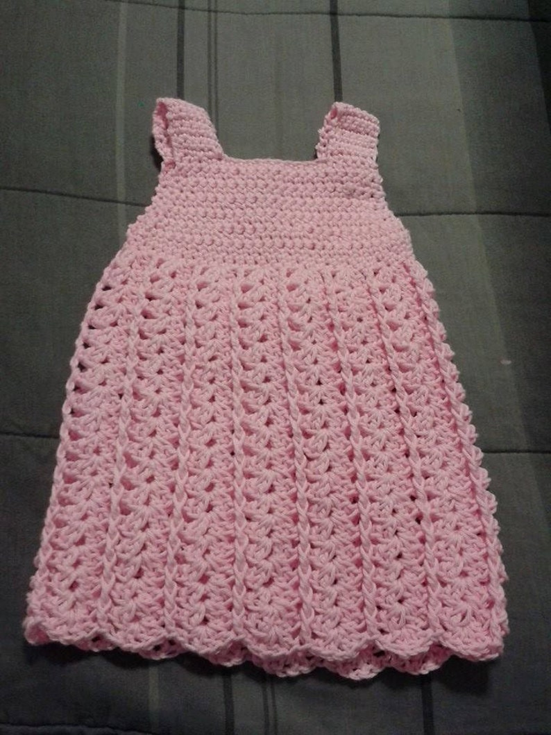 May include: A pink crocheted sleeveless dress with a scalloped hem.