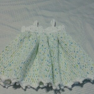 Puede incluir: Un vestido de beb&eacute; blanco de ganchillo con un patr&oacute;n moteado verde y azul.