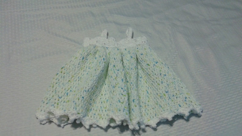 Puede incluir: Un vestido de beb&eacute; blanco de ganchillo con un patr&oacute;n moteado verde y azul.