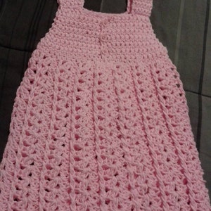 May include: A pink crocheted baby dress with a button closure in the back.