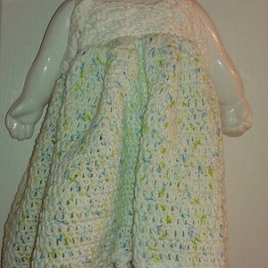 Puede incluir: Mu&ntilde;eca de cer&aacute;mica blanca con un vestido de ganchillo en blanco, azul y verde. El vestido tiene un dobladillo festoneado.