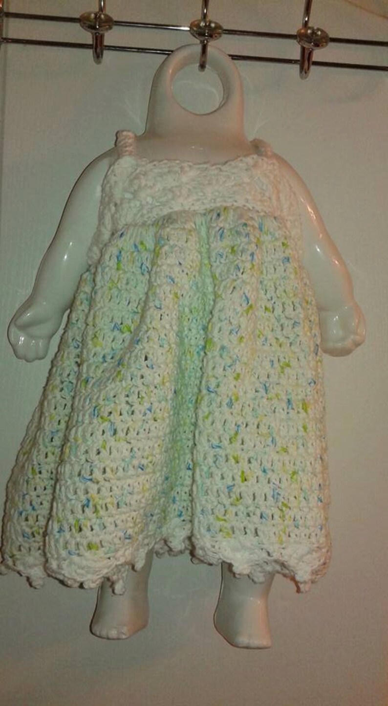 Puede incluir: Mu&ntilde;eca de cer&aacute;mica blanca con un vestido de ganchillo en blanco, azul y verde. El vestido tiene un dobladillo festoneado.