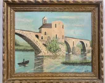 Può includere: Un dipinto incorniciato che raffigura un ponte di pietra su un fiume con un piccolo edificio sul lato sinistro del ponte. Una sola barca con una persona al suo interno è nell'acqua sotto il ponte. Il dipinto è firmato "L.I.P."