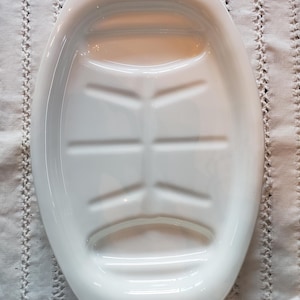 May include: White oval serving platter with a raised center and blue floral accents. The platter has a ridged interior and is likely made of ceramic or porcelain. A decorative piece for serving food.