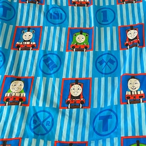 May include: Blue and white striped bedding with a repeating pattern of cartoon train faces in red, green, and blue squares. The design includes train tracks, the letter "T", and the number "1".