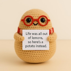 Peut inclure: Une figurine de pomme de terre crochetée, portant des lunettes et une écharpe rouges, tenant une pancarte avec l'inscription "Life was all out of lemons, so here's a potato instead."