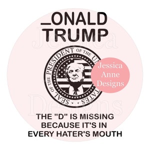 May include: A white circle with a black and white image of a presidential seal with the text "SEAL OF THE PRESIDENT OF THE UNITED STATES" around the outside. The seal features a bald eagle with a banner in its beak that reads "E PLURIBUS UNUM". The seal is surrounded by a ring of stars. The text "_ONALD TRUMP" is at the top of the circle. The text "THE "D" IS MISSING BECAUSE IT'S IN EVERY HATER'S MOUTH" is at the bottom of the circle. A pink circle with the text "Jessica Anne Designs" is in the upper right corner of the circle.