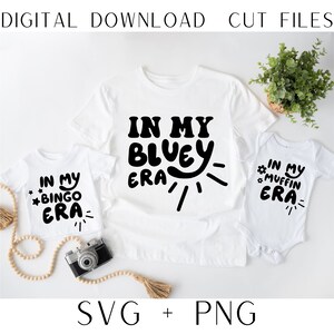 May include: Two white t-shirts with black text. The larger shirt says "In My Bluey Era" with a sun and rays. The smaller shirt says "In My Bingo Era".