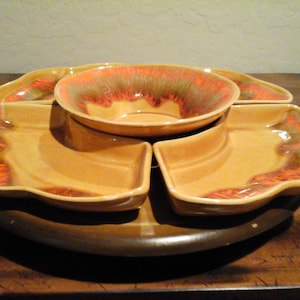May include: A vintage ceramic serving dish with a rotating base and five individual bowls. The bowls are a light brown color with orange and green glaze. The base is a dark brown color.
