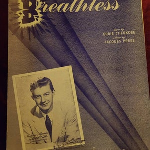 May include: A vintage sheet music cover for the song "Breathless" with lyrics by Eddie Cherkose and music by Jacques Press. The cover features a black and white photo of a man in a white suit and a black tie. The text "Featured and Recorded by Johnny Long and Orchestra" is printed below the photo. The text "Melody Shop Pianos" is printed in the lower right corner of the cover.