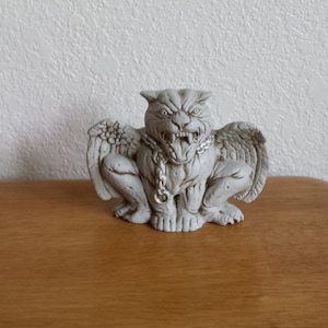May include: A white gargoyle statue with wings, a chain around its neck, and a snarling expression.