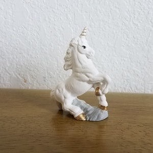 May include: White ceramic unicorn figurine with a gold horn and hooves, standing on a gray base.