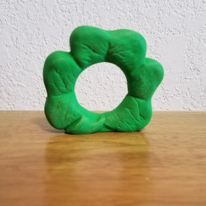 May include: A green four-leaf clover shaped ring made of clay.