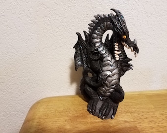 May include: A black and silver dragon figurine with a detailed, textured surface. The dragon has a wide open mouth with sharp teeth and a bright yellow eye.