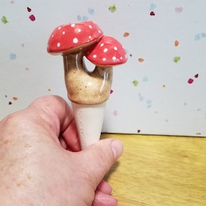 May include: Ceramic mushroom shaped plant waterer with red and white polka dot tops. The waterer is brown with a white base.