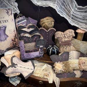 Puede incluir: Una colección de bobinas de cartón con forma de corsé envueltas en diversos encajes y cintas de tela. El conjunto incluye un cartel titulado The Art of Corsetry, un ovillo de cuerda, una pequeña calabaza negra y varios objetos decorativos en tonos morados, beige y negros.