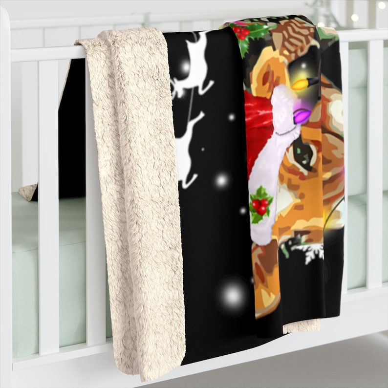 Puede incluir: Una manta de forro polar negra y blanca con un dise&ntilde;o navide&ntilde;o que presenta un reno con un gorro de Pap&aacute; Noel y sosteniendo una cadena de luces. El reno est&aacute; rodeado de copos de nieve y un fondo blanco.